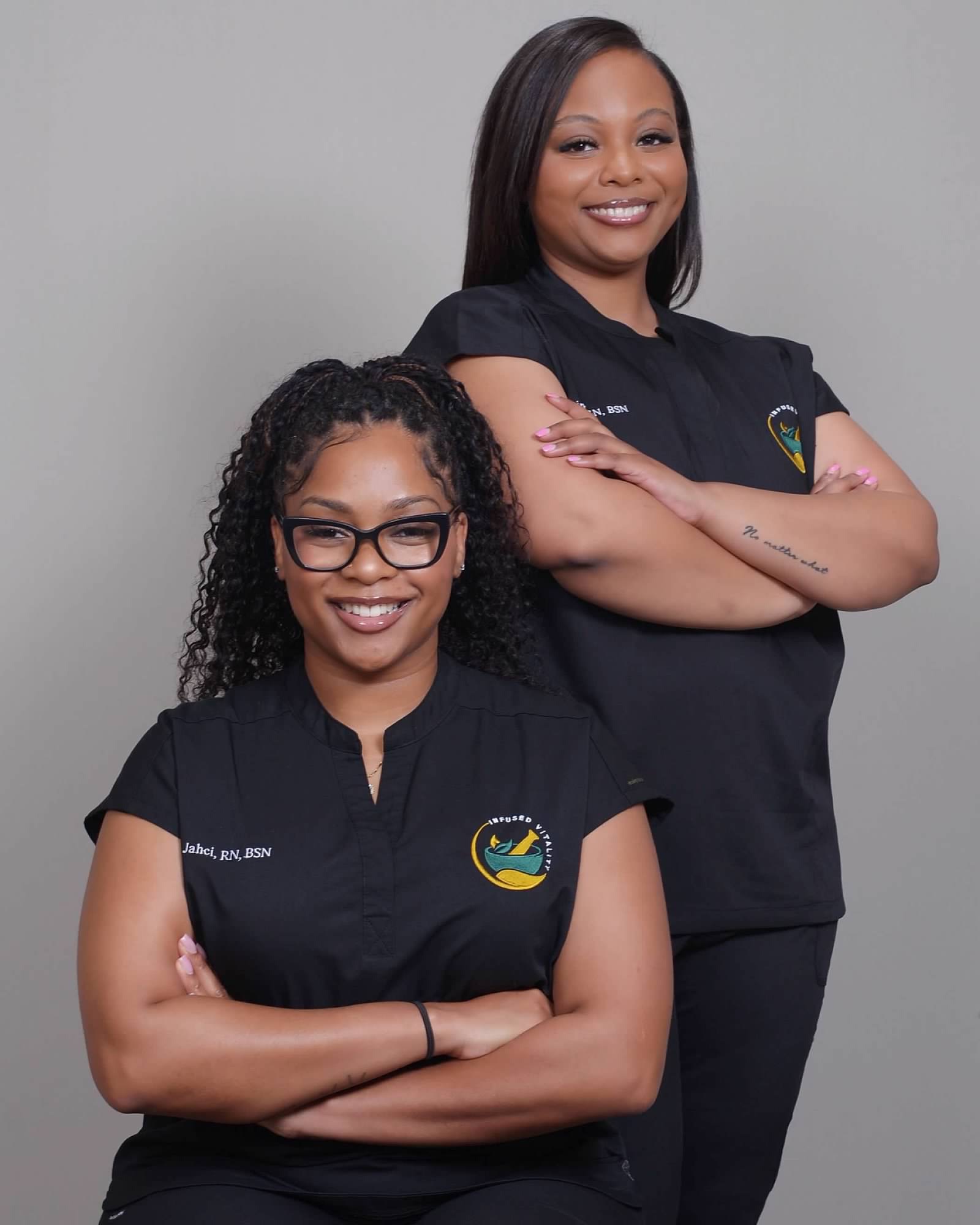 Two healthcare professionals in black scrubs smiling with arms crossed