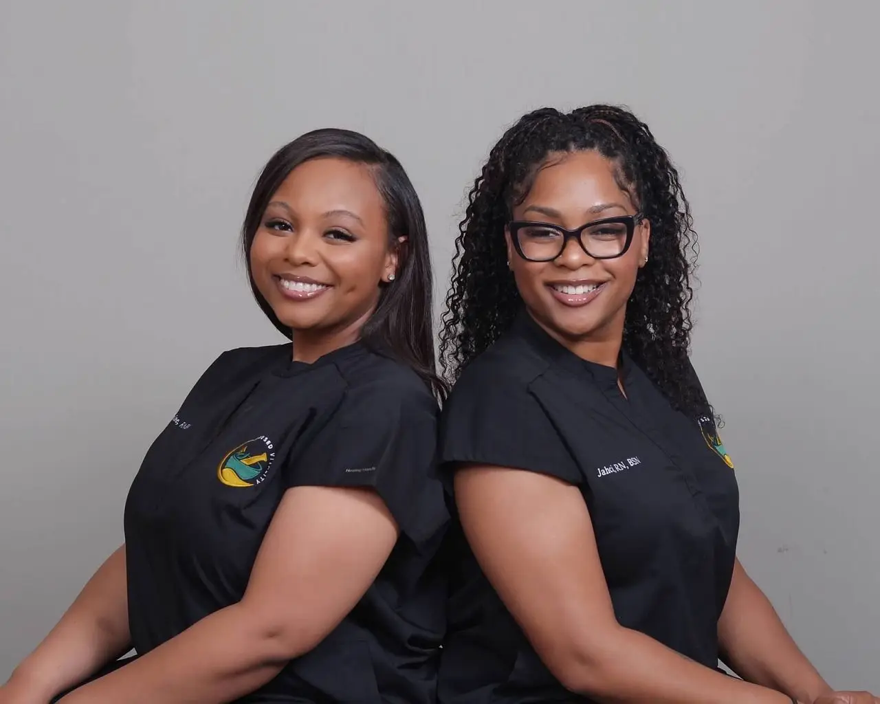 Two healthcare professionals in black scrubs smiling with arms crossed